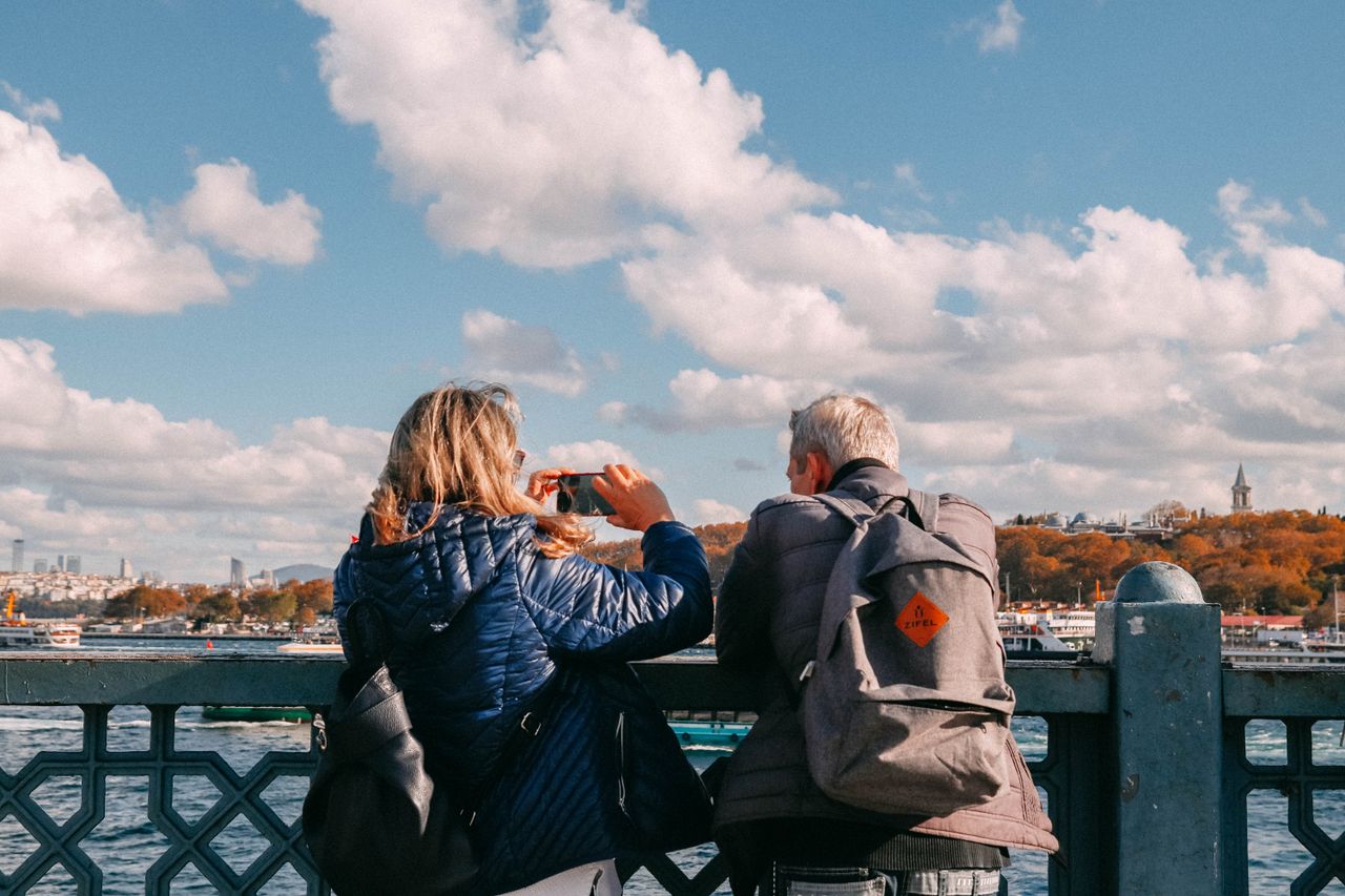 Two adults enjoying the view from a bridge, capturing scenic river sights under a vibrant sky.