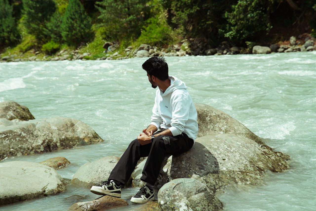 A man sits on rocks by the Lidder River in Pahalgam, enjoying the serene natural surroundings.