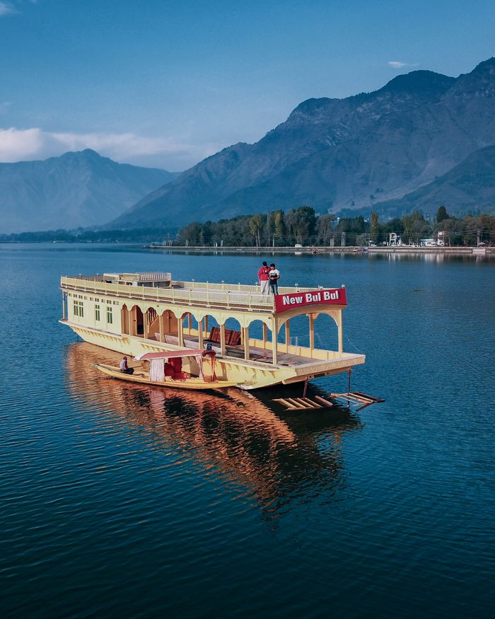 A vibrant houseboat on Dal Lake with stunning mountain backdrop, perfect for travel and leisure.